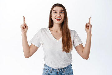 Excited girl shows advertisement on top, looking up with fascinated smiling face, checking out...