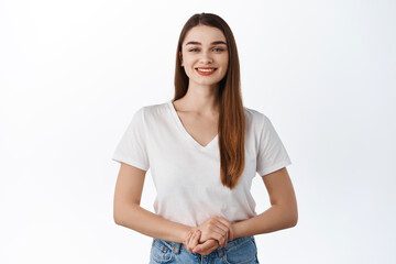 How may I help you. Friendly smiling female student standing in assertive polite pose, ready to assist, talking to client, standing in t-shirt against white background