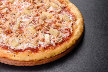 Tasty fresh oven pizza with tomatoes, cheese and pineapple on a dark concrete background