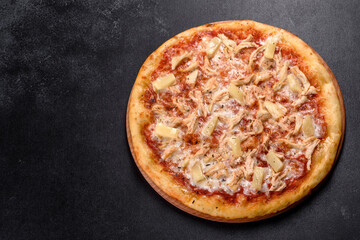 Tasty fresh oven pizza with tomatoes, cheese and pineapple on a dark concrete background