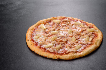 Tasty fresh oven pizza with tomatoes, cheese and pineapple on a dark concrete background