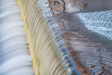Winter landscape of the iced Battle Creek River Cascade captured with motion blur and with reflections of bare trees in calm water, Michigan, USA
