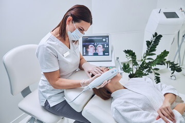 Brunette attractive Caucasian doctor getting facial hydro microdermabrassion peeling in beauty...