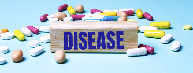 A wooden block with the word DISEASE stands on a blue background among multi-colored pills. Medical concept