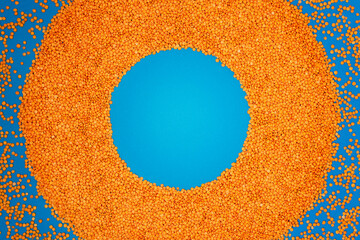 Red lentils are laid out in the form of a round frame on a blue background.