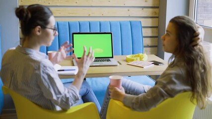 Skilled women colleagues discuss new project looking at monitor of contemporary laptop with green chromakey background in light coworking office