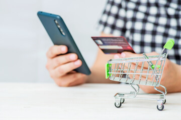 Shopping Cart and woman holding credit card and smartphone shopping online. Woman purchases goods from internet. Female makes payment on bank website