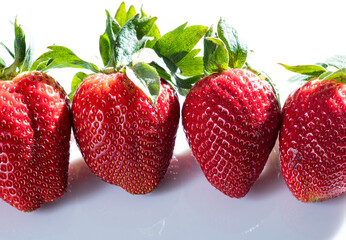 Detail photo of four very red strawberries with their green leaves on a white methacrylate background.