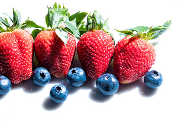 Four very red strawberries with several blueberries on a white background.