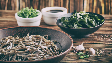 Still life of traditional japanese soba noodles with nori (edible seaweed) and soy sauce, on a wooden surface closeup with selective focus