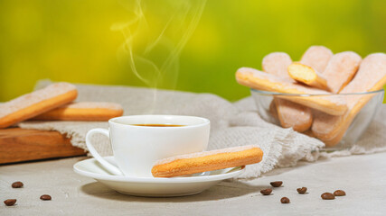 White cup of hot aromatic coffee with steam. Traditional italian savoiardi biscuits or ladyfingers cookies. Selective focus