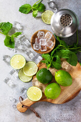 Refreshing cold summer Mojito cocktail making. Mint, lime, ice ingredients and bar utensils on a stone or concrete table. Top view flat lay.