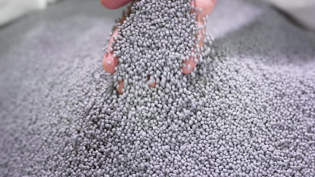 Hands lift polymer granules from a bag in a garbage recycling plant.
