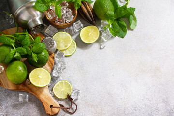 Fototapeta na wymiar Refreshing cold summer Mojito cocktail making. Mint, lime, ice ingredients and bar utensils on a stone or concrete table. Copy space.