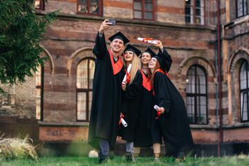 concept of education, graduation. group of happy students in bachelor's robes with diplomas taking a selfie on the phone outdoors.