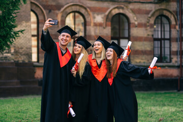 Obraz premium group happy graduates students use mobile phone to take selfie together. After receiving diplomas.