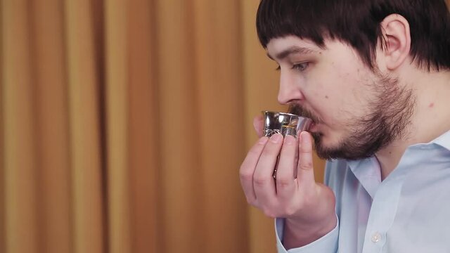 Before the chuppah ceremony, a faceless Jewish groom in the synagogue hall makes a kiddush for wine. Medium plan