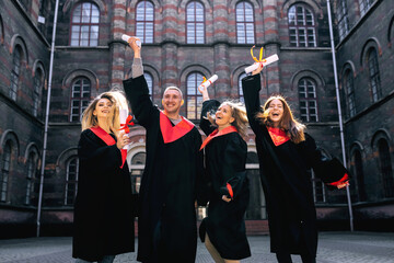 cheerful, contented, students, jumping rejoicing at the end of their studies, holding their hands up with a document.