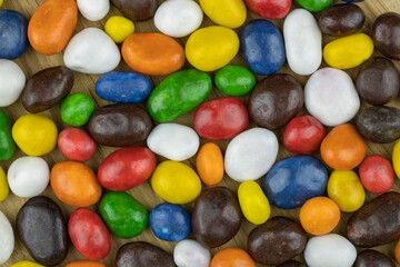 Peanuts in colored chocolate on a wooden board close-up top view.