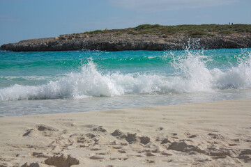 Olas rompiendo en la orilla de una playa de arena con un monticulo de tierra detras con poca vegetación un dia soleado de verano