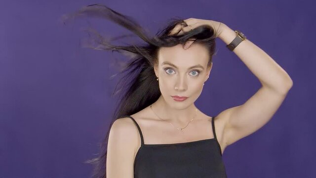 Charming beautiful cute young girl brunette model with beautiful eyes poses for camera and touches wind blowing hair on purple background in foto studio