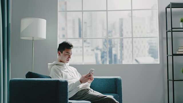 University student man types on grey smartphone on sofa