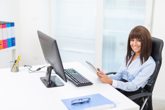 Woman using her tablet in front of her desktop computer