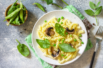 Healthy eating. Pasta fusilli with mushrooms, spinach and green peas on stone table. Vegetarian vegetable mushrooms pasta. Diet menu. Top view flat lay.