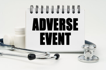On a white table lies a stethoscope, pills and a notebook with the inscription - ADVERSE EVENT