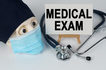 Skull in mask and cap, stethoscope and easel with canvas on which it is written - MEDICAL EXAM