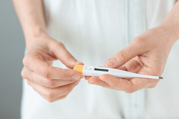 woman's hands holding electronic thermometer on light background. doctor measures temperature, home thermometer measurement, treatment for colds, treatment for coronovirus