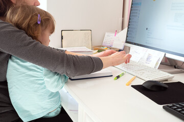 Mother multi-tasking, holding girl kid and using computer at home. Candid authentic and real life mom working and parenting.