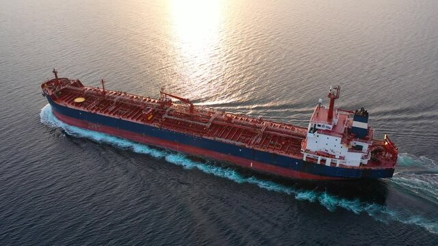 Crude oil tanker underway open sea on sunset time. Sunlight reflected on the water creates a golden shimmering surface. Aerial ocean, close up, natural backlit
