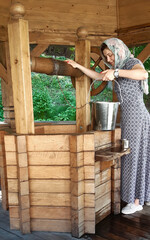 A young girl raises a bucket of water from a wooden well