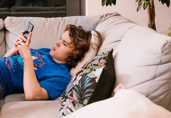 Chłopak młody z telefonem na kanapie. Cyber relaks - obrazy, fototapety, plakaty