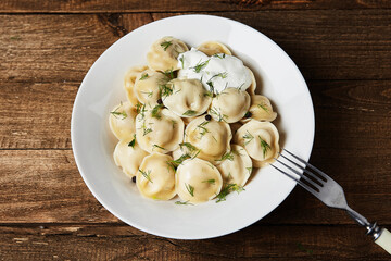 Dumplings with sour cream on a wooden background