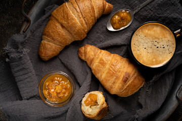 Cup of coffee with a croissant on a dark wooden tray