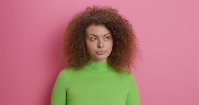 Young displeased woman smirks face has indifferent expression says I am not interested in this has discontent look doesnt like stupid talk keeps arms folded wears green turtleneck poses indoor