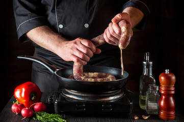 The chef holds the raw meat sausage before cooking. Working environment in restaurant kitchen with vegetables and spices on the vintage table