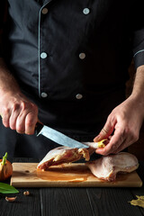 Preparing for cooking chicken legs in the restaurant kitchen. Chef cuts a chicken leg with a knife on cutting board