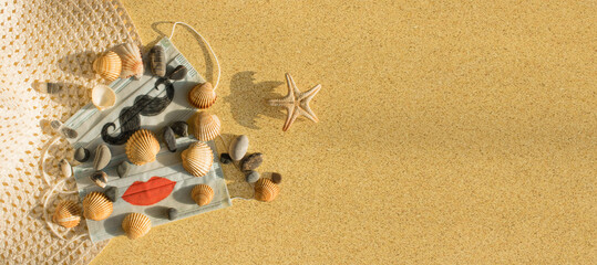 Protective disposable masks with painted mustache and lips, beach hat, starfish, seashells and pebbles backlit by the sun on yellow sand. Travel, vacation and protection against coronavirus