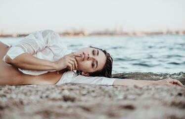 Beautiful woman in white shirt posing on the beach. Young beautiful woman posing at sunset. Summer time concept.