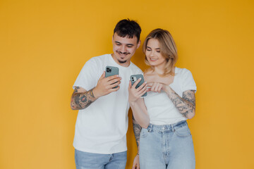 Photo of positive excited people man and woman using mobile phones isolated over yellow background