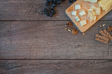 Cheese plate: Em mental, Camembert cheese, Parmesan, Blue cheese, crackers, walnuts, grapes on wooden table. Top view