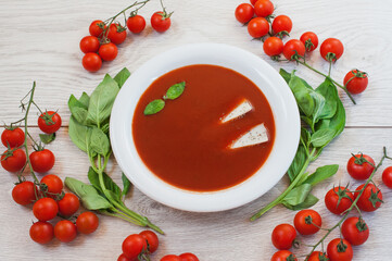 Tomato soup, fresh tomatoes and basil on a wooden background.
