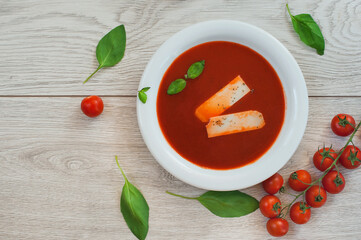 Tomato soup, fresh tomatoes and basil on a wooden background.