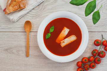 Tomato soup, fresh tomatoes and basil on a wooden background.
