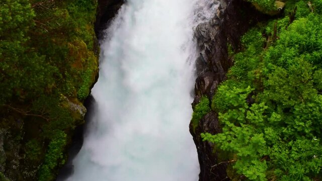 Stormy streams of water of the Slettafossen waterfall, which carved a channel in the rock. Rocky summer landscape of green forest. Norway.