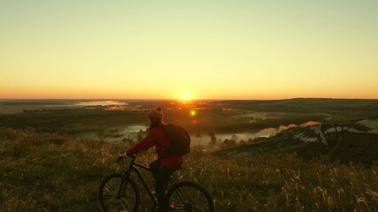 Fototapeta na wymiar The silhouette of a cyclist traveler rides along the edge of the mountain, admiring the landscape and the sunrise. Free tourist rides a bike in nature in the sun. Sports lifestyle. Cyclist exercising
