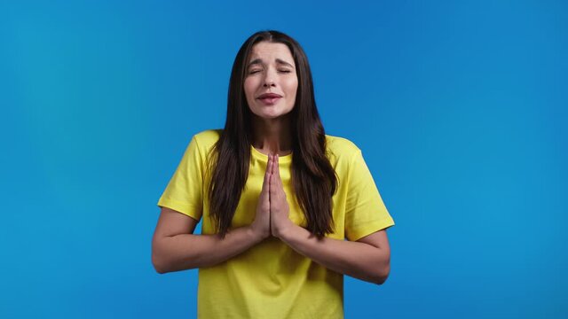 Pretty woman praying with hands on blue background. Girl begging God satisfy her desires, help with.